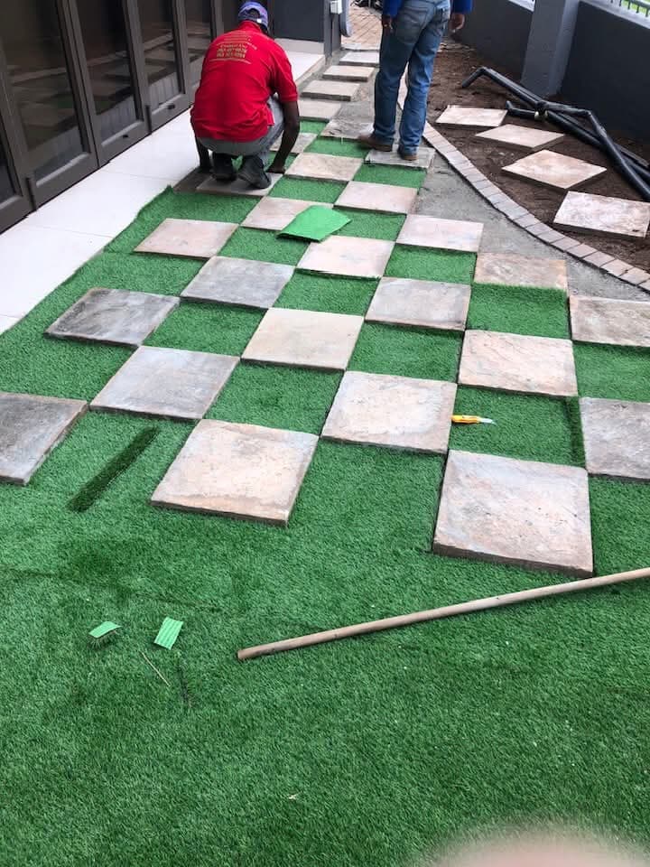 Workers installing checkerboard paver and artificial turf patio
