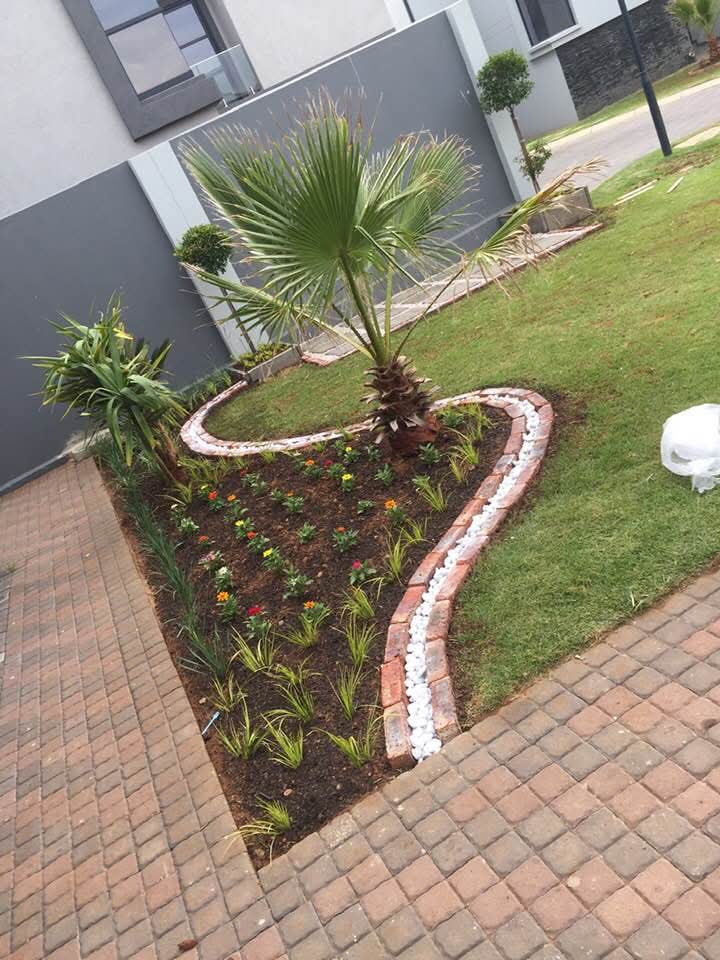 Organic-shaped garden bed with palm tree, flowers and brick edging