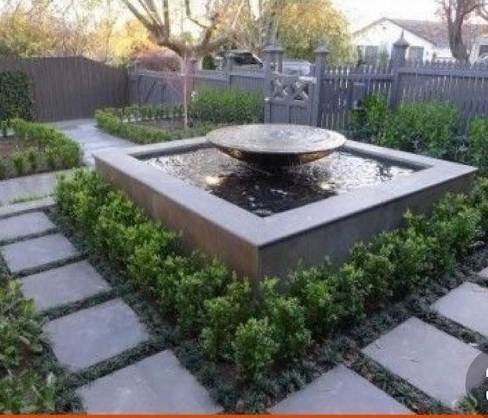 Modern square water fountain with stone pavers and boxwood hedge