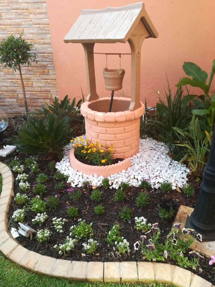 Ornamental wishing well garden feature with flowers and white pebbles