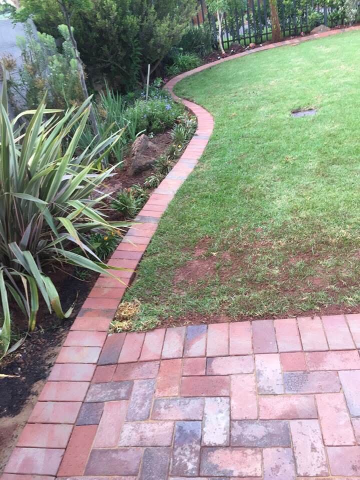 Curved brick border separating patterned patio paving from lawn